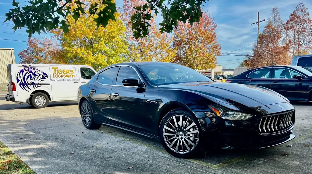 A Tigers Locksmith van parked beside a customer's black Maserati Ghibli under autumn trees